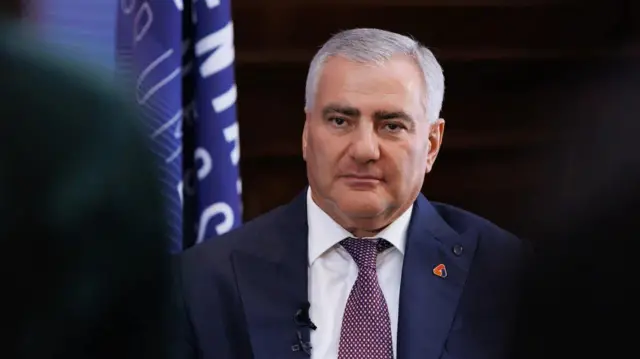 Takım elbiseli Karapetyan kameraya bakıyor. Üzerinde lacivert ceket ve beyaz puantiyeli mor renkli bir kıravat var.