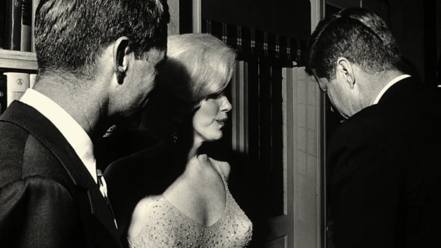 Marilyn Monroe'nun gece elbisesi içinde (ortada) Robert (solda) ve John Kennedy (sağda) ile birlikte, her ikisi de takım elbise giymiş siyah beyaz fotoğrafı. Erkekler kameradan uzağa bakıyor.